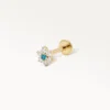 Piercing de cartilage doré en forme de fleur, avec un diamant central bleu et six zircons clairs, vue latérale sur fond blanc.