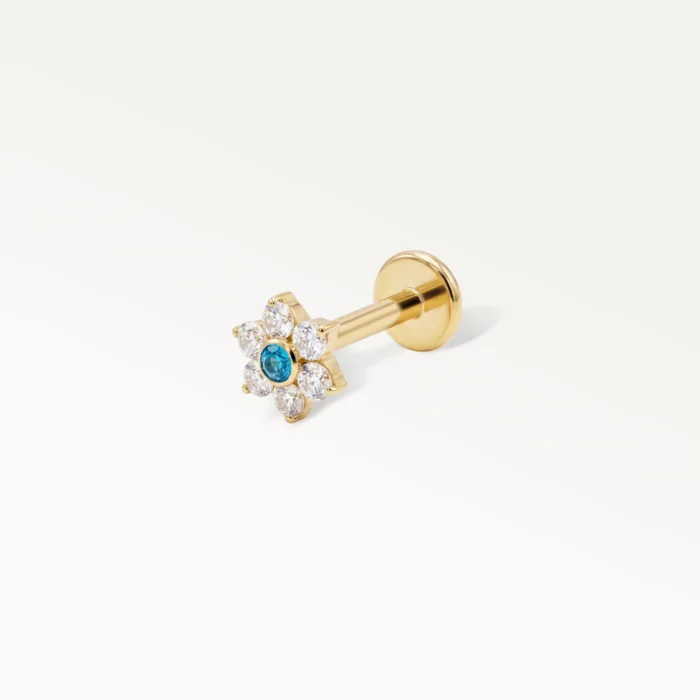 Piercing de cartilage doré en forme de fleur, avec un diamant central bleu et six zircons clairs, vue latérale sur fond blanc.